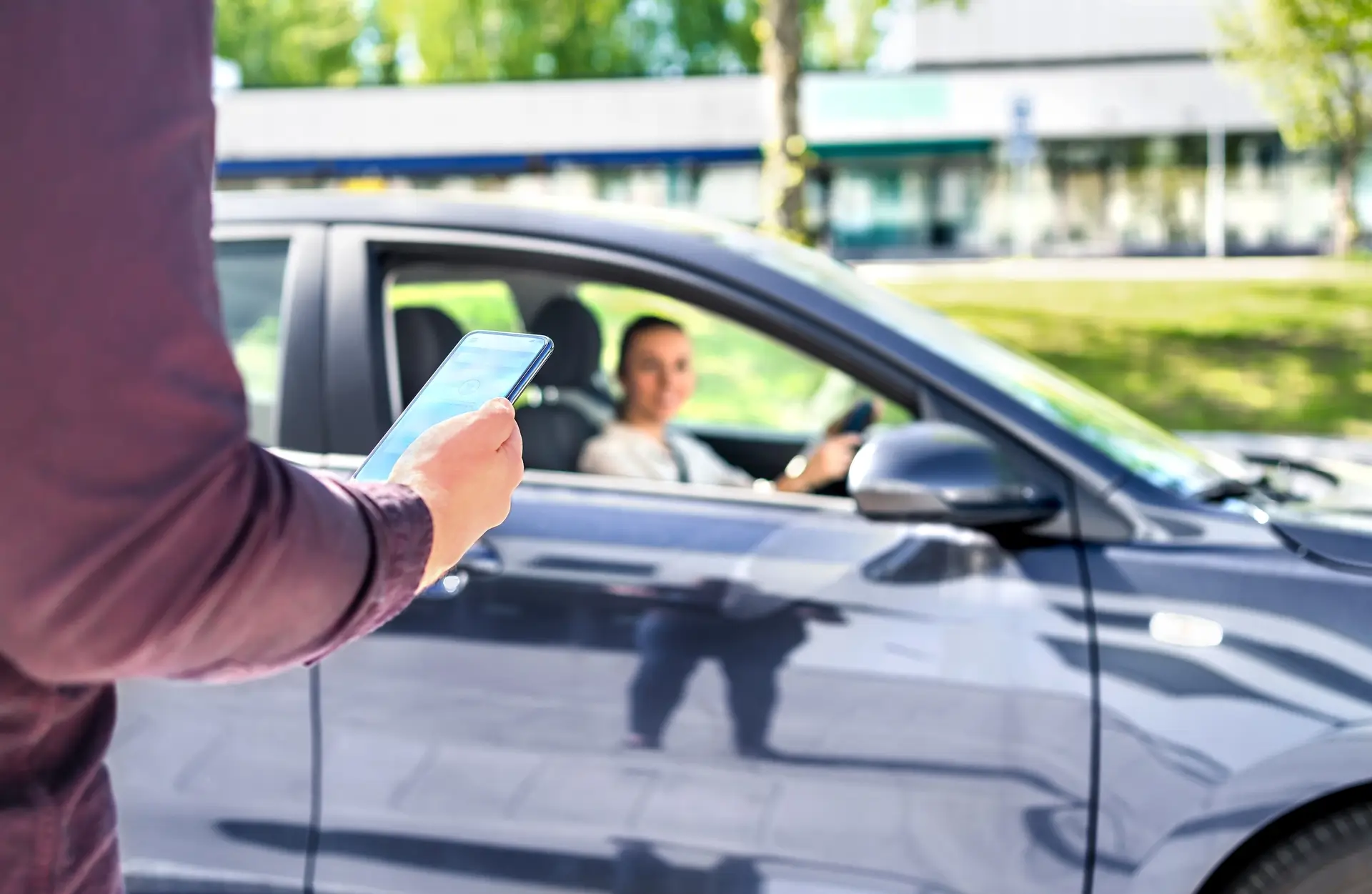 person holding a phone while a driver of a car sits looking at them